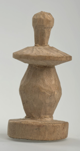 Ujęcie z boku [4]. Ze względu na swój okrągły kształt kolejne ujęcia z boku nie różnią się między sobą znacząco. Pionek został wykonany ręcznie z jednego kawałka jasnego drewna. Na całej powierzchni widoczne są ślady rzeźbienia przy pomocy noża. Obiekt w kolorze naturalnego drewna (nie został pomalowany, ani polakierowany). Krawędź podstawy została dodatkowo obrysowana ołówkiem. Pionek składa się ze spłaszczonej podstawy w formie krążka, części środkowej w kształcie gruszki, spłaszczonego ronda, które zwęża się stopniowo ku górze oraz ku dołowi (przypominając dwa połączone ze sobą talerze, z których każdy skierowany jest dnem do zewnątrz) oraz zwieńczenia o prostej, rozszerzającej się ku górze formie (przypominającej pałkę).