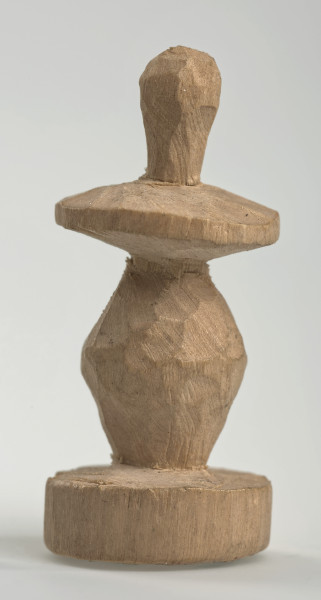 Ujęcie z boku [4]. Ze względu na swój okrągły kształt kolejne ujęcia z boku nie różnią się między sobą znacząco. Pionek został wykonany ręcznie z jednego kawałka jasnego drewna. Na całej powierzchni widoczne są ślady rzeźbienia przy pomocy noża. Obiekt w kolorze naturalnego drewna (nie został pomalowany, ani polakierowany). Od spodu widoczne oznaczenie składające się z dwóch przecinających się ze sobą linii („X”), które umożliwia podzielenie bierek pomiędzy dwóch graczy - wszystkie bierki są jednakowego koloru. Krawędź podstawy została dodatkowo obrysowana ołówkiem. Pionek składa się ze spłaszczonej podstawy w formie krążka, części środkowej w kształcie gruszki, spłaszczonego ronda, które zwęża się stopniowo ku górze oraz ku dołowi (przypominając dwa połączone ze sobą talerze, z których każdy skierowany jest dnem do zewnątrz) oraz zwieńczenia o prostej, rozszerzającej się ku górze formie (przypominającej pałkę).