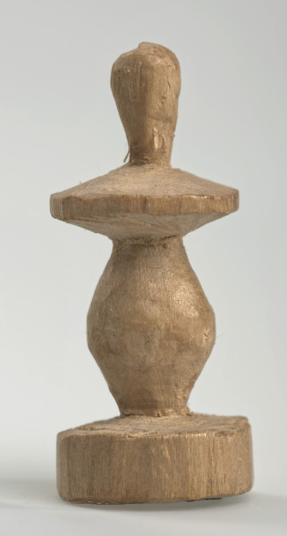 Ujęcie z boku [3]. Ze względu na swój okrągły kształt kolejne ujęcia z boku nie różnią się między sobą znacząco. Pionek został wykonany ręcznie z jednego kawałka jasnego drewna. Na całej powierzchni widoczne są ślady rzeźbienia przy pomocy noża. Obiekt w kolorze naturalnego drewna (nie został pomalowany, ani polakierowany). Od spodu widoczne oznaczenie składające się z dwóch przecinających się ze sobą linii („X”), które umożliwia podzielenie bierek pomiędzy dwóch graczy - wszystkie bierki są jednakowego koloru. Krawędź podstawy została dodatkowo obrysowana ołówkiem. Pionek składa się ze spłaszczonej podstawy w formie krążka, części środkowej w kształcie gruszki, spłaszczonego ronda, które zwęża się stopniowo ku górze oraz ku dołowi (przypominając dwa połączone ze sobą talerze, z których każdy skierowany jest dnem do zewnątrz) oraz zwieńczenia o prostej, rozszerzającej się ku górze formie (przypominającej pałkę).