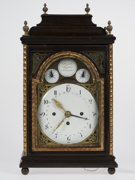 zbliżenie na tarczę zegara ze wskazaniami kalendarza, dni miesiąca, godzinami, kwadransami, minutami i sekundami, z repetierem oraz drewnianą, przeszkloną obudowę z dekoracyjnymi ażurami akustycznymi z mosiądzu grawerowanego