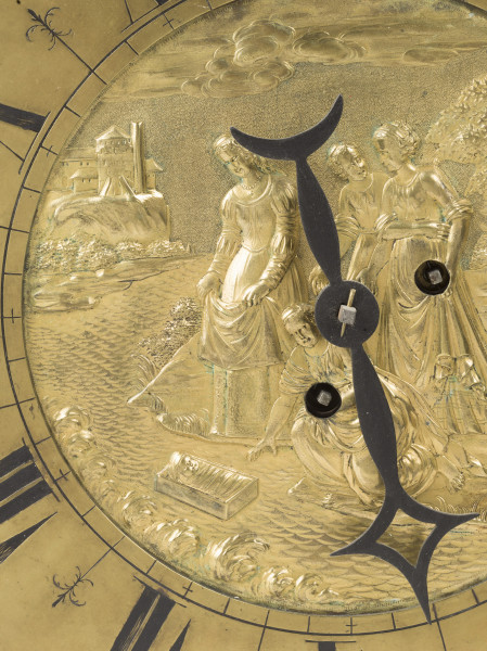 zbliżenie na dekoracyjną tarczę stanowiącą korpus zegara - ozdobiona w centrum płaskorzeźbioną, złoconą sceną biblijną przedstawiającą znalezienie przez córkę faraona małego Mojżesza w koszu płynącym po Nilu