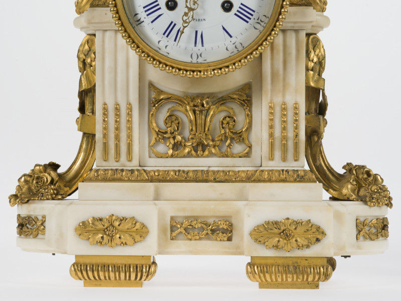 zbliżenie na marmurową powierzchnię obudowy zdobioną dekoracyjnymi elementami z brązu złoconego w kształcie rogów obfitości, stylizowanych, symetrycznych wici roślinnych, rozetek, ozdobnych gzymsów, perełkowania