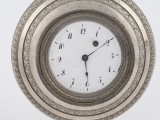 zbliżenie na porcelanową okrągłą tarczę w oprawie z białego metalu, dekorowaną obiegającymi w koło pasami na przemian gładkimi i pokrytymi plastyczną ornamentacją roślinną