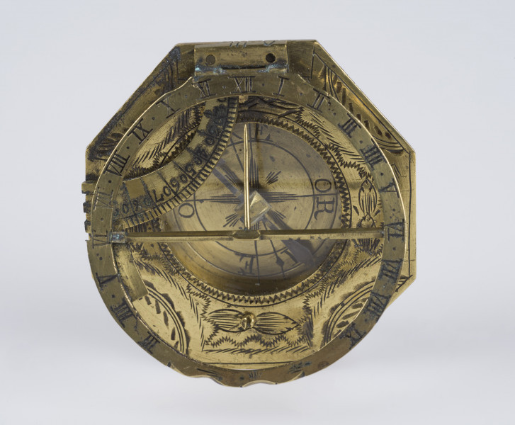 zbliżenie na ośmiokątną, grawerowaną w motywy geometryczno-floralne tarczę zegara z przeszkloną mosiężną puszką z kompasem w części centralnej (szkiełko zamknięte)
