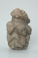 rzeźba; przedmiot obrzędowy; figura kultu zmarłych - Ujęcie prawy bok. Rzeźba o gładkiej powierzchni w szarym steatycie, przedstawiająca postać ludzką o cechach kobiecych, otoczoną piątką mniejszych, dziecięcych sylwetek w różnych pozach.