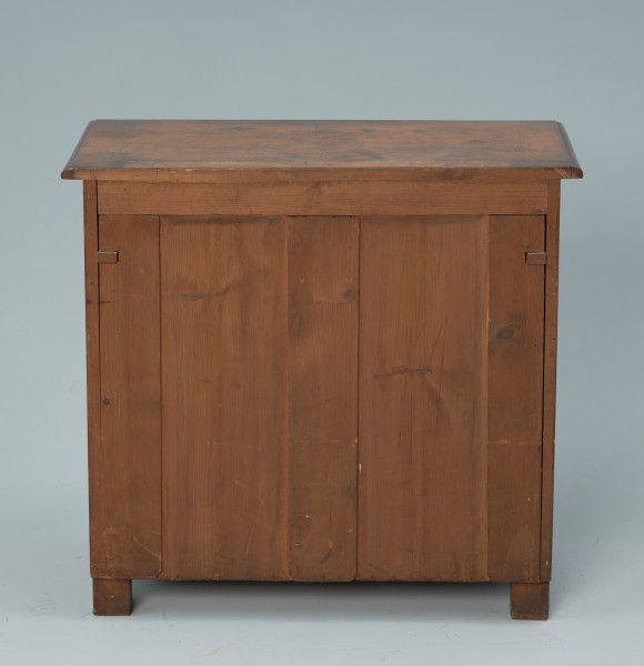 szafka - Ujęcie z tyłu. Szafka w typie bieliźniarki z drewna fornirowanego, przeznaczona pod lustro, dwudrzwiowa z szufladą górną. Tylne nogi proste, klockowe.