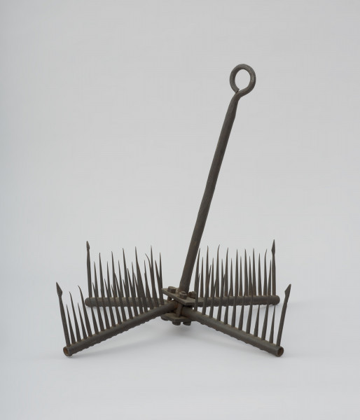 narzędzie kolne - Ujęcie przodu skosem w prawą stronę w pionie. Żelazne narzędzie do połowu węgorzy o formie wyposażonej w zęby kotwicy.
