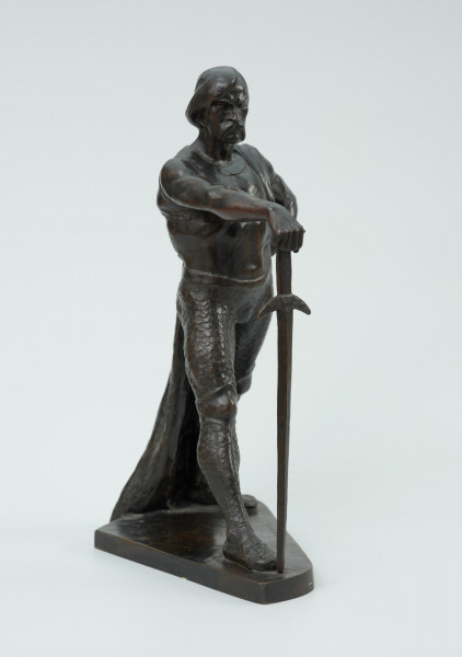 posąg - Ujęcie z przodu skosem w prawą stronę; Postać mężczyzny w postawie kroczącej. Wyciągnięta do przodu prawa ręka wsparta na mieczu. Wysunięta w prawo noga dotyka zakończenia ostrza miecza. Lewa ręka zgięta, dłoń wsparta na biodrze. Przez lewe ramię przewieszona draperia której zwój opada za lewą nogą do podstawy. Twarz pociągła, silnie zarysowane łuki brwi, usta okolone opadającym wąsem. Rozczesane gładko włosy.