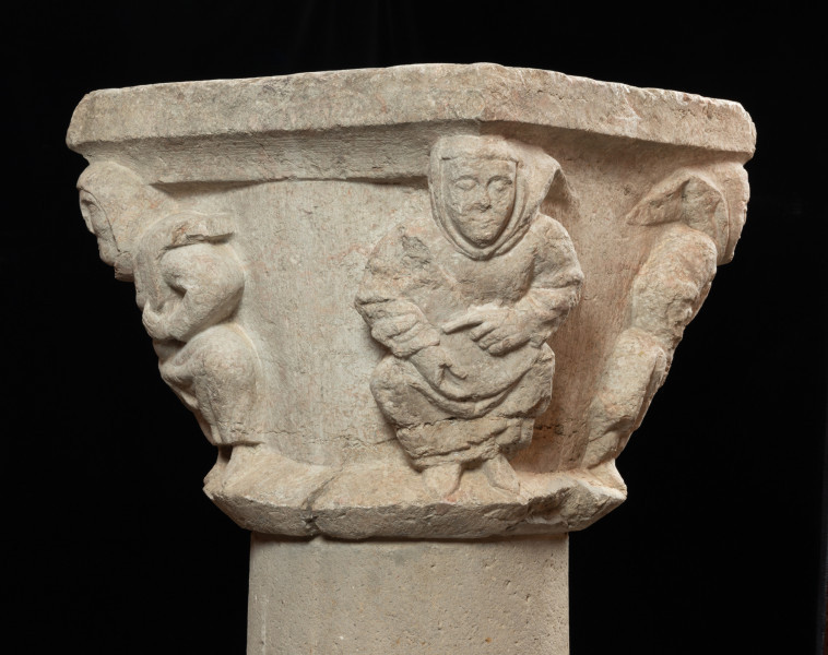 Kapitel z przedstawieniem czterech mnichów - atlantów - Ujęcie czwartego boku skosem. Kapitel blokowo-kielichowy, rozszerzający się ku górze, wykuty z jednego kawałka kamienia. Okrągłą podstawę otacza wałek o trójkątnym profilu. Zwieńczenie w formie szerokiej czworobocznej płyty abakusa. W narożnikach kapitela płaskorzeźbione wizerunki czterech mnichów. Postaci o krępej budowie ukazane frontalnie, w pozycji przykucniętej. Stopami opierają się o dolny wałek, głowami podpierają abakus. Relief głęboki, półplastyczny, światłocieniowy. Gładko opracowane tło. Niewielkie uszczerbienia zwłaszcza w partii abakusa i dolnego wałka. Pod spodem centralne wgłębienie do umocowania trzpienia łączącego kapitel z trzonem.