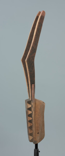 maska - Ujęcie lewego boku. Drewniana, rzeźbiona maska antylopy, z dużymi geometrycznymi otworami na oczy.