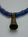biżuteria, naszyjnik - Ujęcie detalu. Zamknięty, kobaltowy naszyjnik. Na bawełnianym sznurku znajdują się nałożone szklane, kobaltowe paciorki oraz wykonany z brązu wisiorek w kształcie wydłużonego stożka przypominającego dzwon. Wisiorek ozdobiono wzorami geometrycznymi.