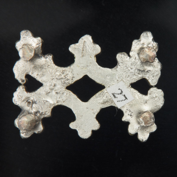 Pozłacane okucie pasa z ornamentem lilijkowym i akantem - Ujęcie z tyłu. Okucie pasa, prostokątne, sześcioramienne, uformowane z dwóch symetrycznych części połączonych w osi wzdłużnej. Od spodu obrobionego mniej starannie niż z przodu i bez złocenia - w narożnikach przylutowane cztery płaskie, okrągłe, sklepane nity. Pozioma rysa grawerska w postaci myślnika.