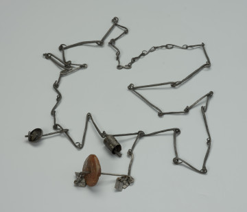 przedmiot ceremonialny, przedmiot religijny i obrzędowy, fetysz - Ujęcie z przodu. Łańcuch składający się z licznych, połączonych ze sobą żelaznych ogniw. Rozdwaja się na końcu tworząc literę Y. Ozdobiony pierścieniami z podwójnym wisiorkiem o trapezowatym kształcie, kamiennym i żelaznym paciorkiem oraz otwartym, żelaznym walcem.