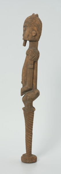 drewniana, rzeźbiona figura - Ujęcie z lewego boku. Drewniana, rzeźbiona postać człowieka na szczudłach.