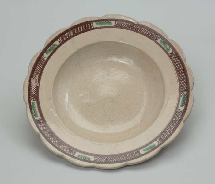 talerz - Ujęcie z góry. Talerz płaski uformowany na kole garncarskim z gliny o barwie jasnobrązowej , szkliwiony tylko po wewnętrznej stronie. Dno lekko wyodrębnione, korpus niewysoki przechodzi w plaski, szeroki wylew zakończony faliście ( 