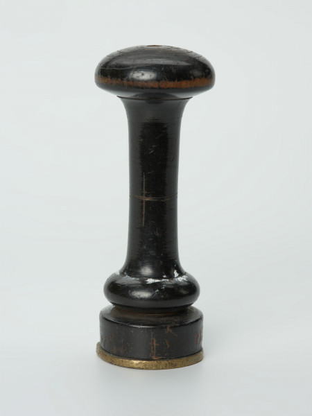 tłok pieczętny - Ujęcie w pionie tyłu tłoka pieczęcią w dół. Okrągły tłok pieczętny z brązu z drewnianym uchwytem oraz rysunkiem kroczącego gryfa w polu pieczęci.