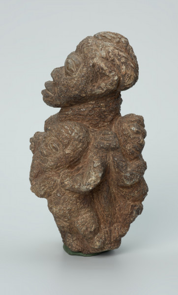 rzeźba; przedmiot obrzędowy; figura kultu zmarłych - Ujęcie lewy bok. Rzeźbiona w ziemistym steatycie siedząca postać ludzka o cechach kobiecych, otoczona przez trójkę mniejszych, dzieciecych postaci, skierowanych ku niej z uniesionymi rękoma.