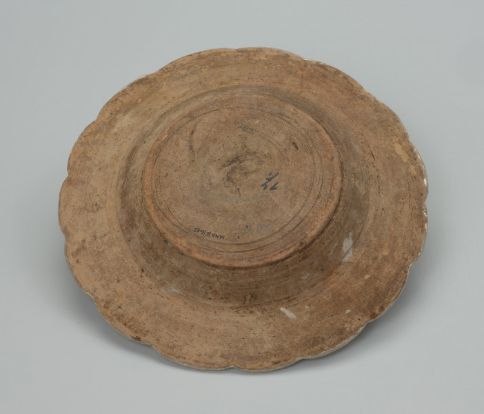 talerz - Ujęcie spodu. Talerz płaski uformowany na kole garncarskim z gliny o barwie jasnobrązowej , szkliwiony tylko po wewnętrznej stronie. Dno lekko wyodrębnione, korpus niewysoki przechodzi w plaski, szeroki wylew zakończony faliście ( 