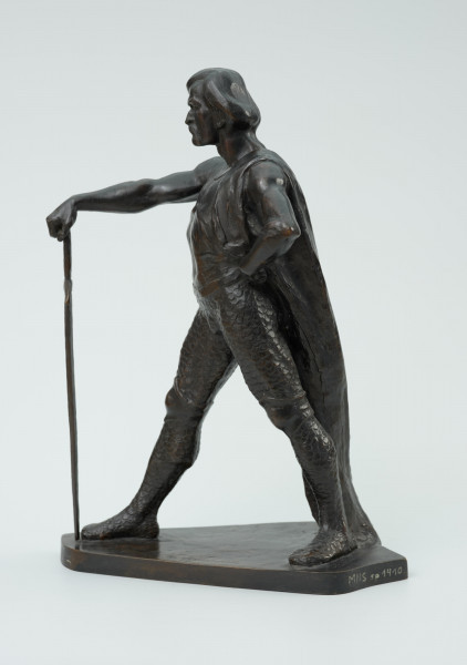 posąg - Ujęcie z boku z lewej strony; Postać mężczyzny w postawie kroczącej. Wyciągnięta do przodu prawa ręka wsparta na mieczu. Wysunięta w prawo noga dotyka zakończenia ostrza miecza. Lewa ręka zgięta, dłoń wsparta na biodrze. Przez lewe ramię przewieszona draperia której zwój opada za lewą nogą do podstawy. Twarz pociągła, silnie zarysowane łuki brwi, usta okolone opadającym wąsem. Rozczesane gładko włosy.