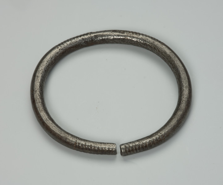 biżuteria, bransoleta - Ujęcie z przodu z dołu. Otwarta, żelazna, okrągła bransoleta ozdobiona nacięciami w postaci pionowych linii oraz wgłębieniami w kształcie maleńkich kropek. Zamknięcie bransolety w formie szpary.