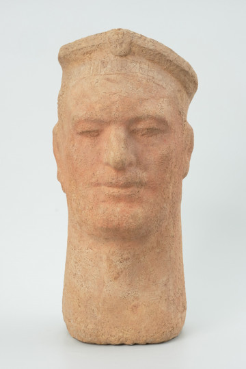 portret męski - Ujęcie z przodu; Głowa męska o miękkim modelunku. Twarz pociągła, nos prosty, usta wydatne. Długa, mocna szyja. Na głowie marynarska czapka z emblematem pośrodku, nad czołem.