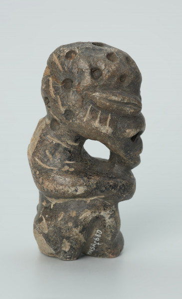 rzeźba; przedmiot obrzędowy; Figura kultu zmarłych - Ujęcie prawy bok. Rzeźbiona w grafitowobeżowym steatycie siedząca postać ludzka, której nieproporcjonalnie dużą głowę zdobią liczne, okrągłe wgłębienia, natomiast ciało pokrywają pionowe i ukośne nacięcia, oznaczające prawdopodobnie skaryfikację. Powierzchnia rzeźby z rysami, mikropęknięciami, przetarciami oraz drobnymi uszkodzeniami.
