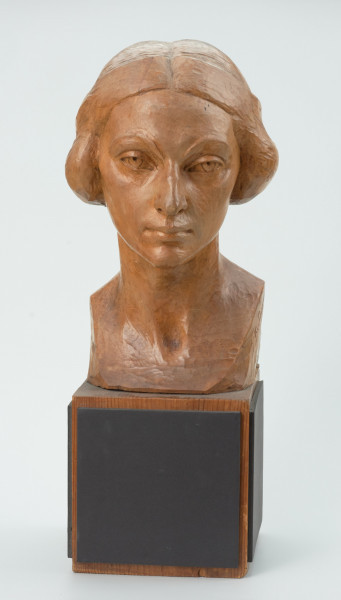 głowa - Ujęcie z przodu; Głowa młodej kobiety. Twarz owalna, podbródek spiczasty, duże nieco skośne oczy pod wyrazistymi łukami brwi. Krótkie przylegające włosy z przedziałkiem pośrodku.