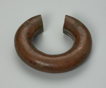 biżuteria, bransoleta - Ujęcie z tyłu z góry. Bransoleta miedziana o owalnym kształcie. Ozdobiona tłoczonymi, geometrycznymi wzorami, w postaci trójkątów, zygzaków, maleńkich kwadracików oraz punktowymi nacięciami. Wzory naniesiono na stronie zewnętrznej bransolety, przy jej otwarciu, na bocznych grzbietach.