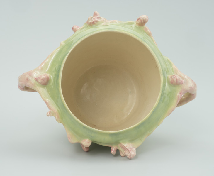 ceramika - Ujęcie wnętrza; Gładkie wnętrze wazonu w kolorze kremowym. Na zewnątrz widoczne cząstki postaci, na jasnym zielonym tle malowanego wazonu.