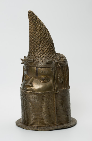 Głowa Królowej Matki - Ujęcie z przodu lewej strony. Brązowy, pusty w środku odlew głowy kobiety, o złotym zabarwieniu. Twarz o cechach negroidalnych, wydatnych, lekko rozchylonych ustach oraz szerokim u nasady nosie ma oczy z wyraźnie zaznaczoną linią powiek. Na ich wysokości usytuowane są nieduże uszy. Lekko wypukłe czoło dekorowane jest pionowymi inkrustacjami z żelaza oraz trzema podłużnymi, symetrycznie rozmieszczonymi, pogrubieniami nad każdym okiem. Szyję i podbródek do wysokości dolnej wargi zasłonięto masywnym naszyjnikiem z korali. Głowa jest nienaturalnie poszerzona w tylnej części, tuż pod przechyloną do przodu koroną o charakterystycznym kształcie dziobu papugi, którą nad uszami ozdobiono dwoma rozetami. W dolnej części korony widnieje pięć ozdób o walcowatej formie, trzy nad czołem, dwie za rozetami oraz opaska z korali. Tuż za koroną znajduje się duży, owalny otwór na rzeźbiony kieł słonia, którego brak. Poniżej, po obu stronach twarzy i z tyłu głowy, zaznaczono zaplecione w warkoczyki włosy. Z tyłu głowy pomiędzy włosami a naszyjnikiem usytuowany jest niewielki, okrągły otwór. U podstawy odlewu znajduje się pozioma listwa, dekorowana motywem plecionki.