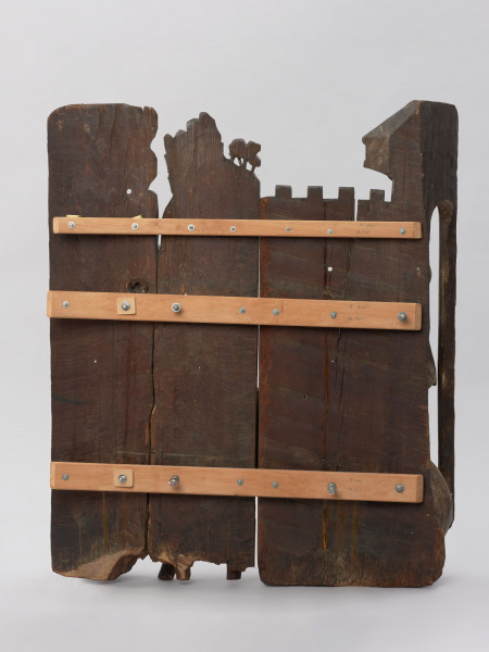 sztuka sakralna, kwatera ołtarza, płaskorzeźba - Ujęcie z tyłu; Płaskorzeźba przedstawiająca Chrystusa pochylonego pod ciężarem krzyża oraz pomagającego mu na rozkaz żołnierzy Szymona Cyrenejczyka. Scena na tle pejzażu górskiego przed murami miasta. Kwatera środkowa późnogotyckiego ołtarza pasyjnego z Wkryujścia (Ueckermünde).