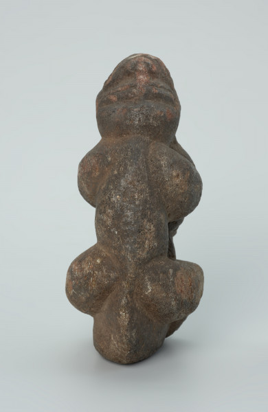 rzeźba; popiersie; Figura kultu zmarłych - Ujęcie z tyłu. Rzeźbione w grafitowobeżowym steatycie popiersie człowieka z jaszczurką, której łapy obejmują głowę i ramiona postaci ludzkiej.