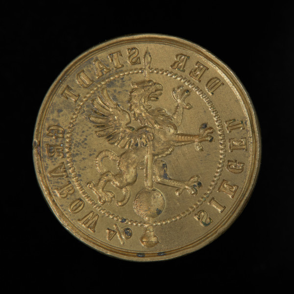 tłok pieczętny - Ujęcie przodu pieczęci. Okrągły tłok pieczętny z brązu z trzpieniem montarzowym w formie ostrosłupa oraz rysunkiem gryfa na iglicy wieży w polu pieczęci.