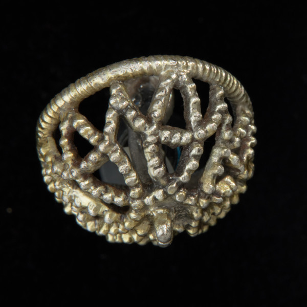 Pozłacany ażurowy guz koszyczkowy - Ujęcie od spodu. Pozłacana okragła ozdoba, koszyczkowa, ażurowa, w formie kopułki.  Na wierzchołkach wypustki uformowane w oczka. Czterolistna rozeta wykonana jest z taśmy. W centrum nieregularny guzek.