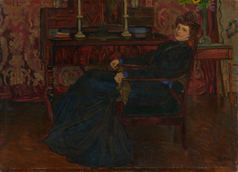 portret kobiecy - ujęcie z przodu; Kompozycja w kształcie leżącego prostokąta. Dominantę barwną stanowią zróżnicowane walorowo brązy i czerwienie. Fragment wnętrza pokoju, w centrum postać kobieca siedząca w zwróconym w lewą stronę, obitym materią fotelu. Kobieta odziana w długą suknię, ukazana z profilu, głowa en trois quarts. W tle wzorzysta, dekoracyjna makata, stylowe biurko z książkami i parą lichtarzy. Z prawej strony stolik z szufladą, na którym stoi wysoki, szklany flakon z bukietem kwiatów.