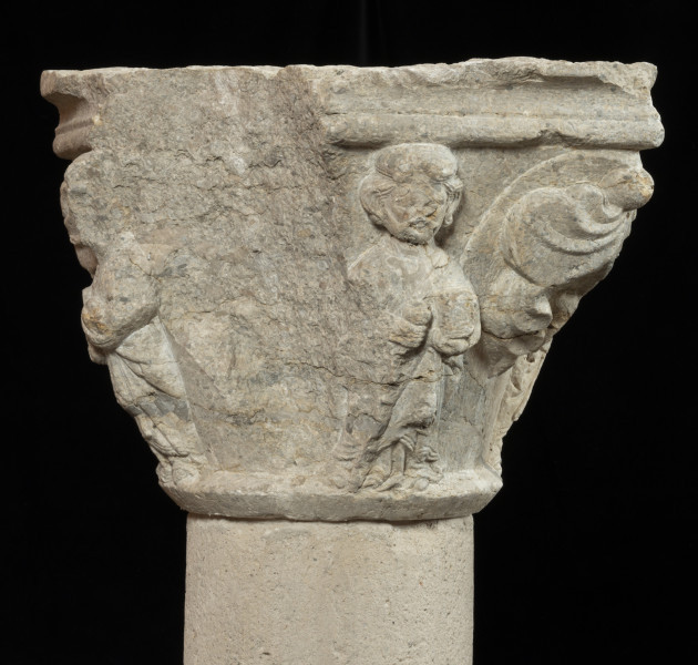 kapitel z przedstawieniem czterech apostołów - Ujęcie z pierwszym apostołem częściowo uszkodzone. Kapitel blokowo-kielichowy, rozszerzający się ku górze, wykuty z jednego kawałka kamienia. Okrągłą podstawę otacza wałek o profilu trójkątnym. Zwieńczenie w formie szerokiej czworobocznej płyty abakusa o krawędziach profilowanych wałkiem i wklęską. Na osi każdego boku półplastyczne przedstawienie frontalnie ukazanych postaci Apostołów: Piotra, Pawła, Bartłomieja i Jakuba Starszego. Pomiędzy nimi duże liście palmetowe dekoracyjnie ułożone na narożnikach. Postaci o dużych głowach i dość smukłej budowie, trzymają atrybuty. Długie tuniki i płaszcze o pofałdowanej powierzchni przylegają do sylwetek. Charakterystyczne zdobienie krawędzi szat podwójnym wałkiem i symetrycznie ułożone falujące fryzury. Relief półplastyczny, światłocieniowy. Tło opracowane gładko. Jedno z naroży kapitela uszkodzone. Liczne pęknięcia i ukruszenia na powierzchni kamienia. Pod spodem centralne wgłębienie do umocowania trzpienia łączącego kapitel z trzonem.