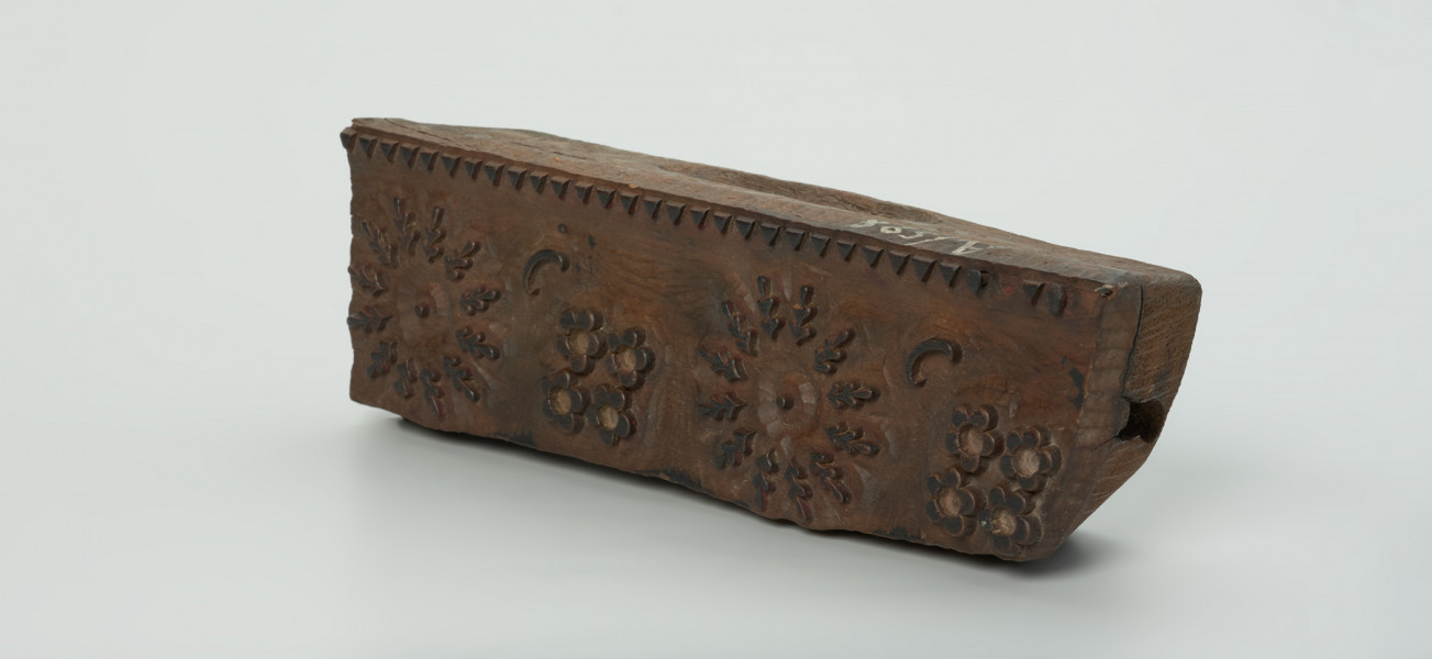 sprzęt do drukowania i grafiki, matryca drukująca - Ujęcie przodu skosem w prawą stronę Matryca do drukowania tkanin z wykonanym w drewnie ornamentem o motywie geometryczno - roślinnym.