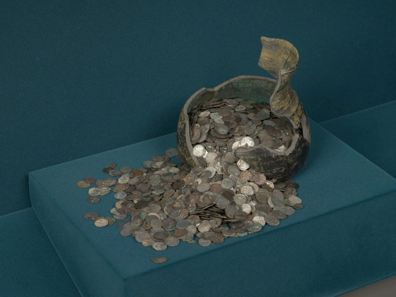 skarb monet - Ujęcie z przodu. Fragment glinianego naczynia z wysypującymi się z niego monetami. Skarb 2588 monet, głównie denarów pomorskich, ukryty w naczyniu glinianym po 1405-1410 roku.