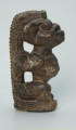 rzeźba; przedmiot obrzędowy; Figura kultu sił wegetacji - Ujęcie prawy bok. Rzeźbiona w grafitowym steatycie, siedząca na owalnej podstawie, postać ludzka, którą od tyłu obejmuje postać zoomorficzna o cechach jaszczurki.