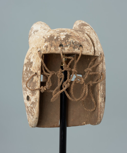 maska - Ujęcie z tyłu. Drewniana, rzeźbiona maska pantery. Głowa zaokrąglona, zwieńczona trójkątnymi, lekko skierowanymi do przodu uszami. Wycięte prostokątne oczy, mały spłaszczony nos. Pysk szeroki, wypukły z widocznymi rzeźbionymi zębami. Całość biała, miejscami przybrudzona. W części tylnej maski wywiercone otwory, umożliwiające przymocowanie jej do twarzy tancerza oraz pozostałości po sznurku.