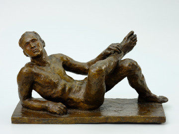 akt męski - Ujęcie z przodu; Rzeźba nagiej postaci męskiej. Mężczyzna lezy wsparty na prawym łokciu i przedramieniu. Lewa noga jest zgięta w kolanie. Prawa noga jest podniesiona i wsparta na lewej nodze. Lewa ręka przytrzymuje  prawą nogę w tej pozycj. Twarz jest skierowana ku widzowi. Rzeźba wykonana z brązu.