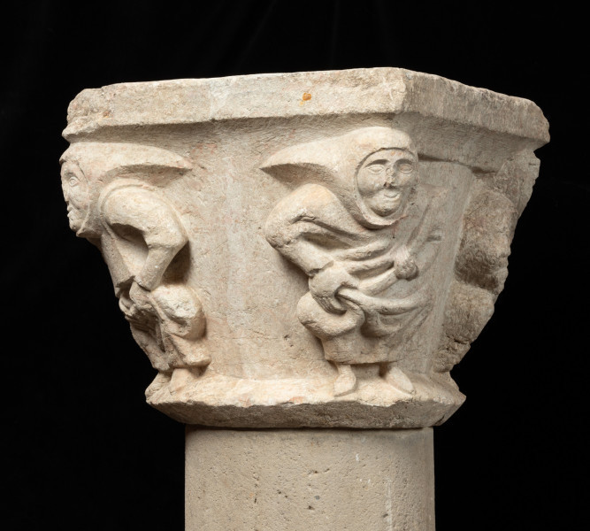 Kapitel z przedstawieniem czterech mnichów - atlantów - Ujęcie trzeciego boku. Kapitel blokowo-kielichowy, rozszerzający się ku górze, wykuty z jednego kawałka kamienia. Okrągłą podstawę otacza wałek o trójkątnym profilu. Zwieńczenie w formie szerokiej czworobocznej płyty abakusa. W narożnikach kapitela płaskorzeźbione wizerunki czterech mnichów. Postaci o krępej budowie ukazane frontalnie, w pozycji przykucniętej. Stopami opierają się o dolny wałek, głowami podpierają abakus. Relief głęboki, półplastyczny, światłocieniowy. Gładko opracowane tło. Niewielkie uszczerbienia zwłaszcza w partii abakusa i dolnego wałka. Pod spodem centralne wgłębienie do umocowania trzpienia łączącego kapitel z trzonem.