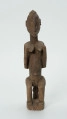 drewniana, rzeźbiona figura - Ujęcie z przodu. Drewniana, rzeźbiona figura kobiety siedzącej na stołku.