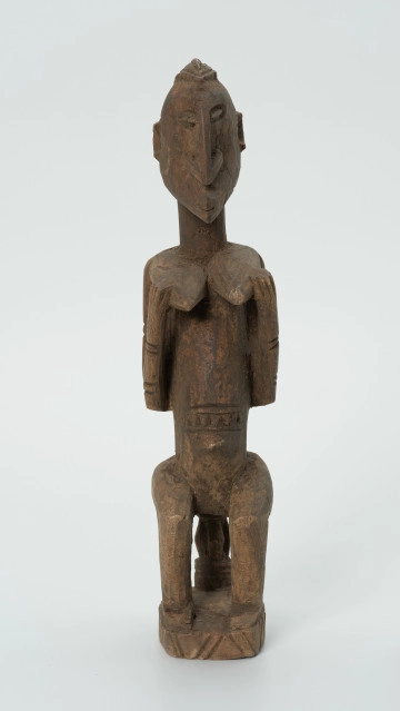 drewniana, rzeźbiona figura - Ujęcie z przodu. Drewniana, rzeźbiona figura kobiety siedzącej na stołku.