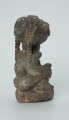 rzeźba; przedmiot obrzędowy; Figura kultu sił wegetacji - Ujęcie prawy bok. Rzeźbiony w grafitowym steatycie, na owalnej podstawie, mężczyzna w pozycji siedzącej z opaską przedstawioną za pomocą wypukłego ornamentu kostkowego, której końce opadają na ramiona i plecy postaci.