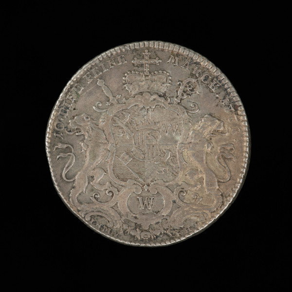 talar - Ujęcie rewersu. Na rewersie monety pod koroną na tle skrzyżowanego pastorału i miecza barokowa czteropolowa tarcza herbowa trzymana przez dwa lwy z małą ukoronowaną tarczą w centrum, powyżej napis i znaki mincerskie. Na rancie motyw wieńca laurowego.