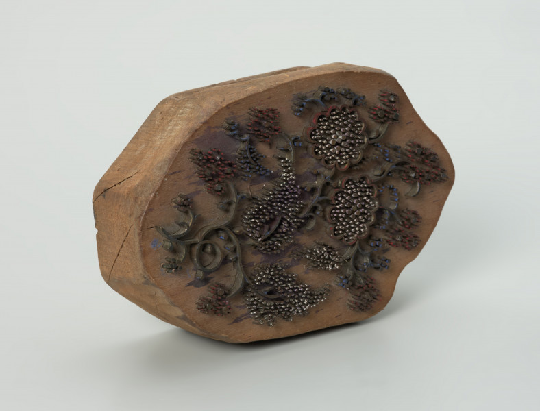 sprzęt do drukowania i grafiki, matryca drukująca - Ujęcie przodu skosem w lewą stronę. Matryca do drukowania tkanin z wykonanym z nabitych w drewno mosiężnych sztyfcików i blaszek ornamentem o motywie roślinnym.