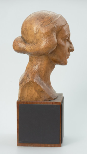 głowa - Ujęcie z boku z prawej strony; Głowa młodej kobiety. Twarz owalna, podbródek spiczasty, duże nieco skośne oczy pod wyrazistymi łukami brwi. Krótkie przylegające włosy z przedziałkiem pośrodku.