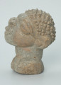 rzeźba; głowa; figura kultu zmarłych - Ujęcie lewy bok. Rzeźbiona w szarobeżowym steatycie, usadowiona na okrągłej podstawce, głowa postaci ludzkiej z dużymi uszami z tyłu i w charakterystycznym uczesani w formie małych, lekko zaokrąglonych stożków, być może loczków.