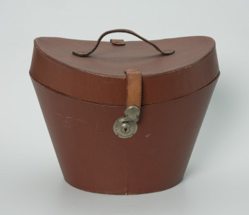owalny futerał do kapelusza - Ujęcie z przodu; Owalny futerał do kapelusza. Owalne, rozszerzające się ku górze pudło z pokrywą o zagłębionej formie z uchwytem w centrum. Pokrywa zamykana na zamek kluczykowy.